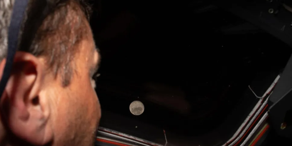 Artemis 2 commander Reid Wiseman gazes through the window of the Orion capsule Integrity at the Moon, appearing as a small bright dot against the darkness of deep space, during the historic lunar flyby on April 6, 2026.